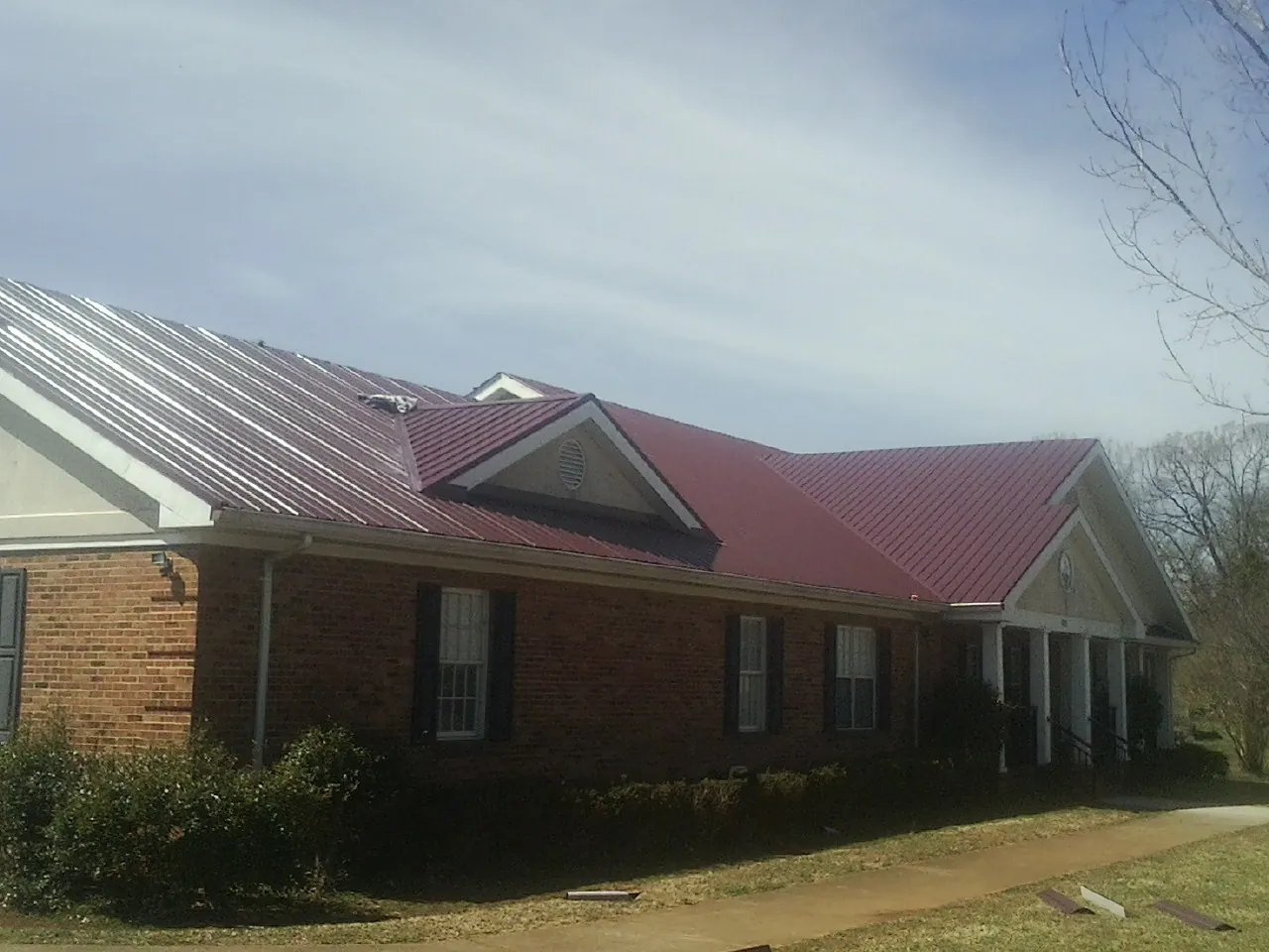 Red metal roof with gabled entries on a long brick building, from a Hail Damage Roof Repair job in Barnwell