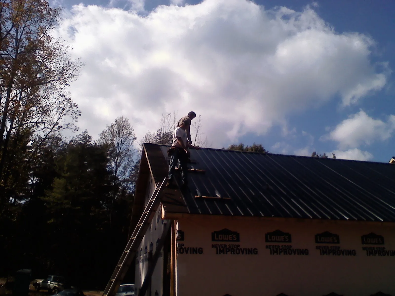 Roofer fastening dark metal panels high against a cloudy sky, from a Roof Inspection job in Barnwell