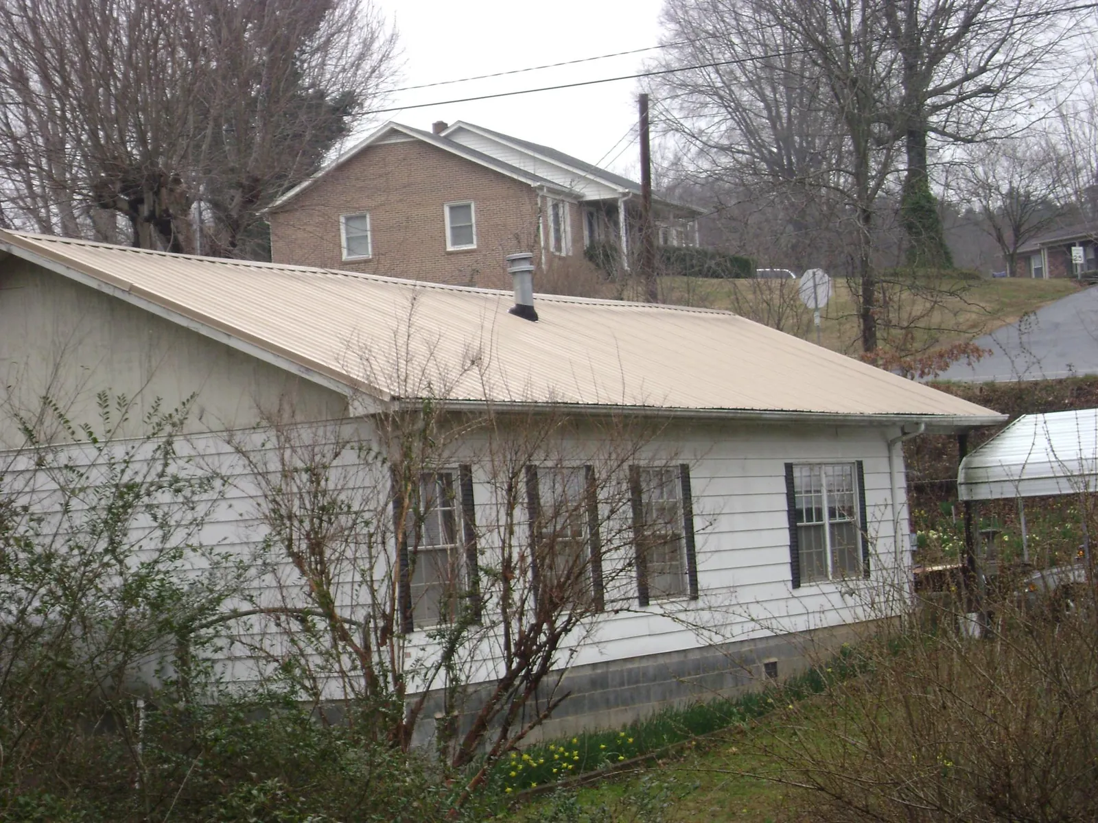 Tan metal roof on a white sided house set into a hillside — Commercial Roofing by Roofing Brothers in Barnwell
